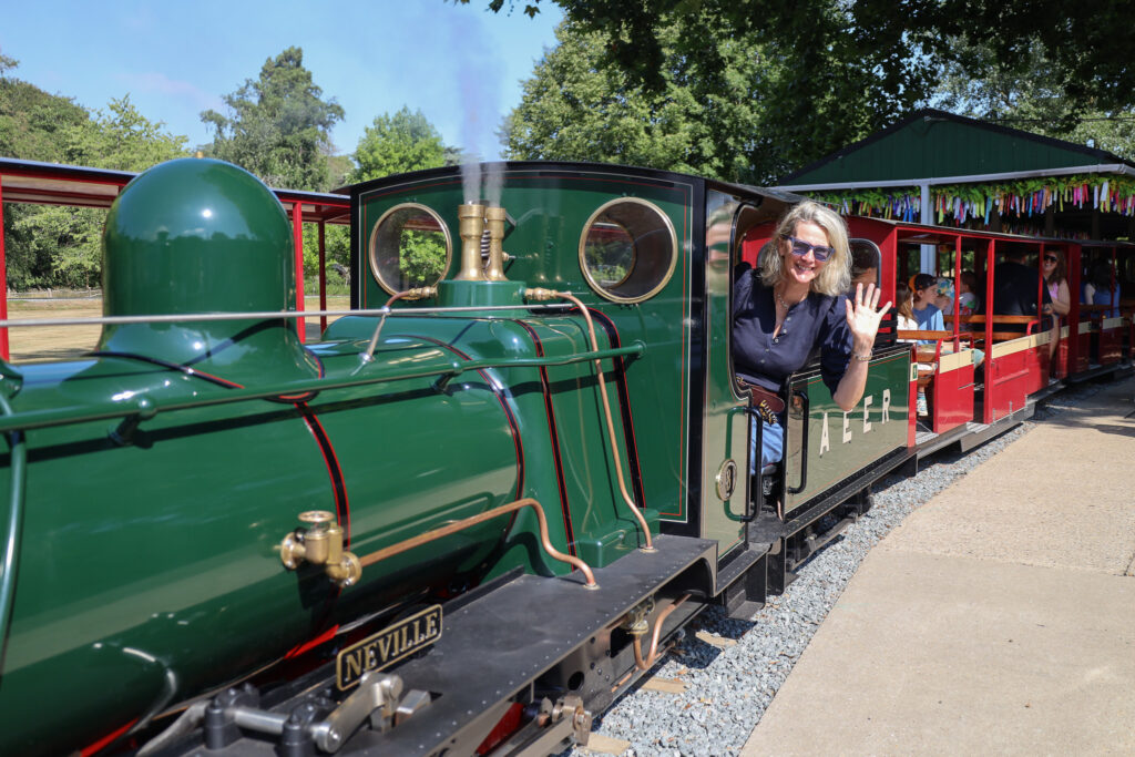 Visitors enjoying a ride on the miniature railway at Audley End Enchanted Railway, with a green steam locomotive at the station.
