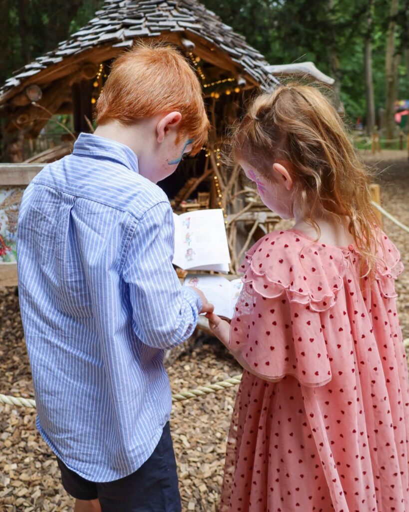 Two children following the Fairy and Elf Walk at Audley End Enchanted Railway's Summer Festival, reading a magical trail book in the woodland.