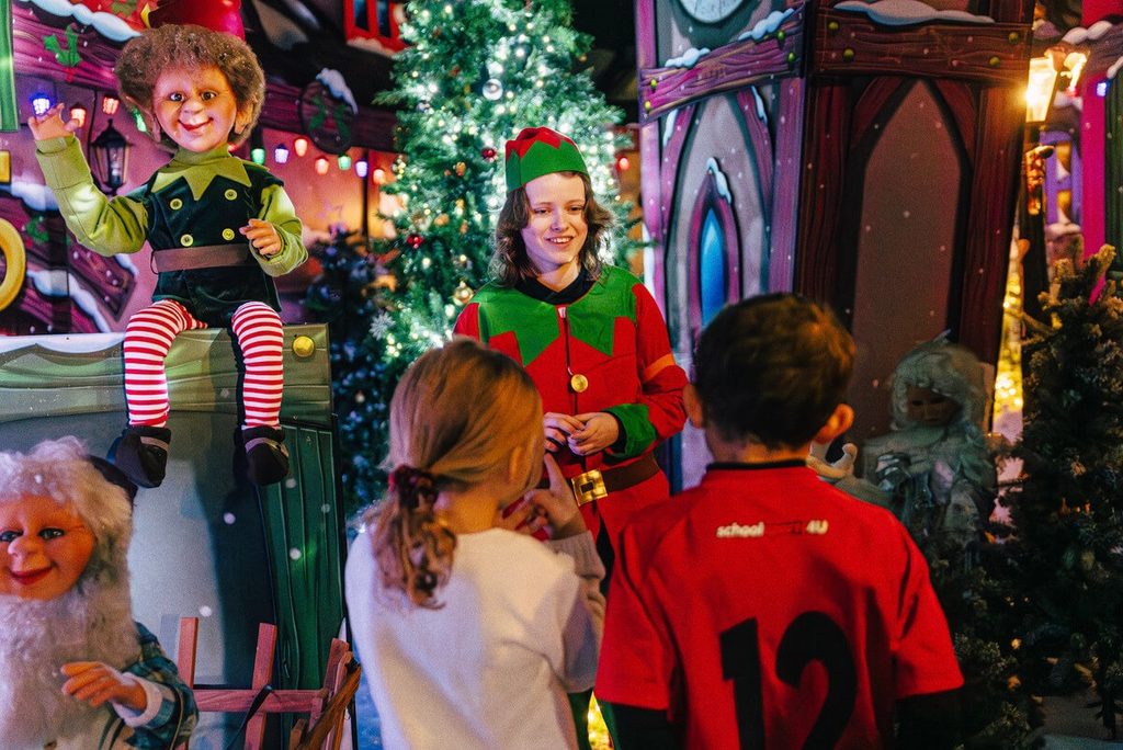 Two children meeting a Christmas elf at Audley End Enchanted Railway’s Christmas Special in Essex, surrounded by magical festive decorations, twinkling Christmas trees and colourful woodland characters.