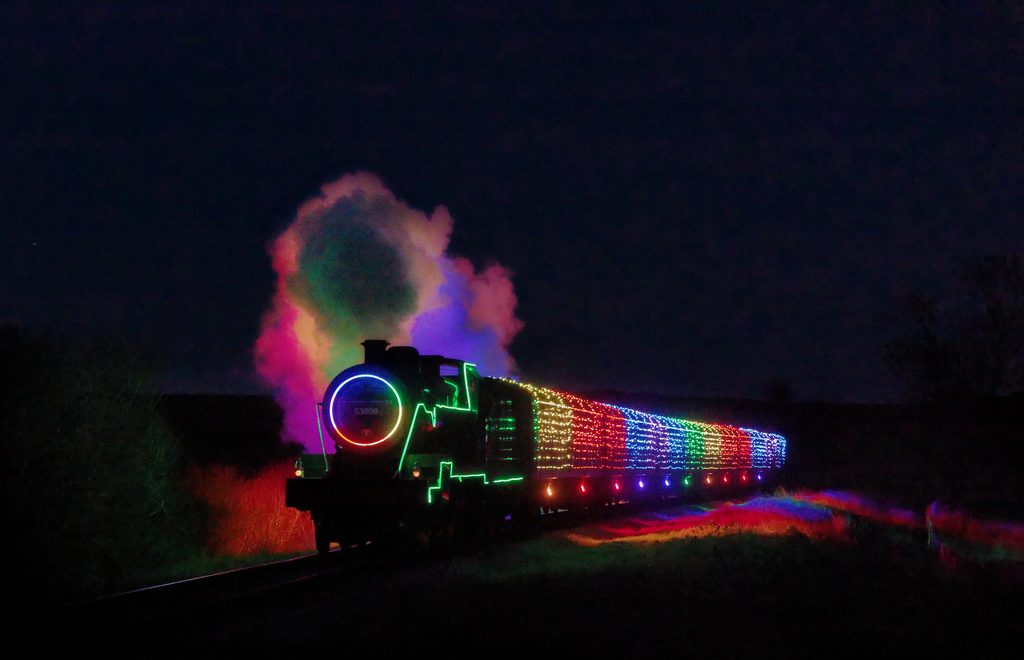 Steam train wrapped in colourful Christmas lights at night time.