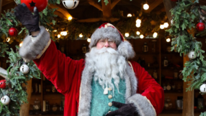 Father Christmas smiling and waving in wooden lodge.